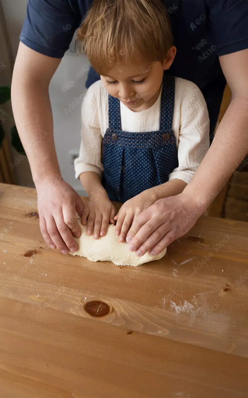 Ein Erwachsener und ein Kind kneten gemeinsam Teig auf einem Holztisch.